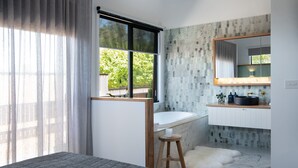 Un baño moderno con un amplio ventanal, un lavabo blanco y un taburete de madera.