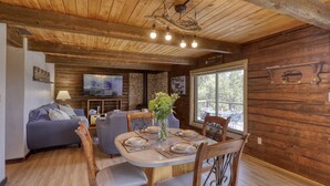 A cozy cabin interior with a dining area, a sofa, and a television.