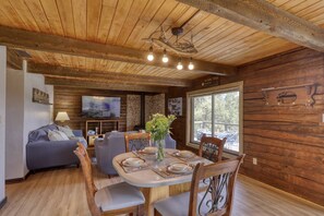 A cozy cabin interior with a dining area, a sofa, and a television.