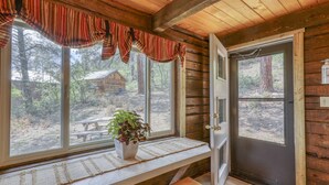 A cabin with a wooden interior, a bench, a potted plant, and a view of a wooden structure outside.