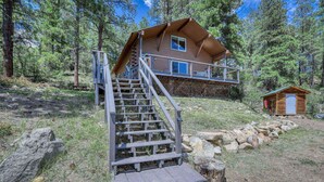 A cabin with a wooden staircase leading to a deck, surrounded by trees.