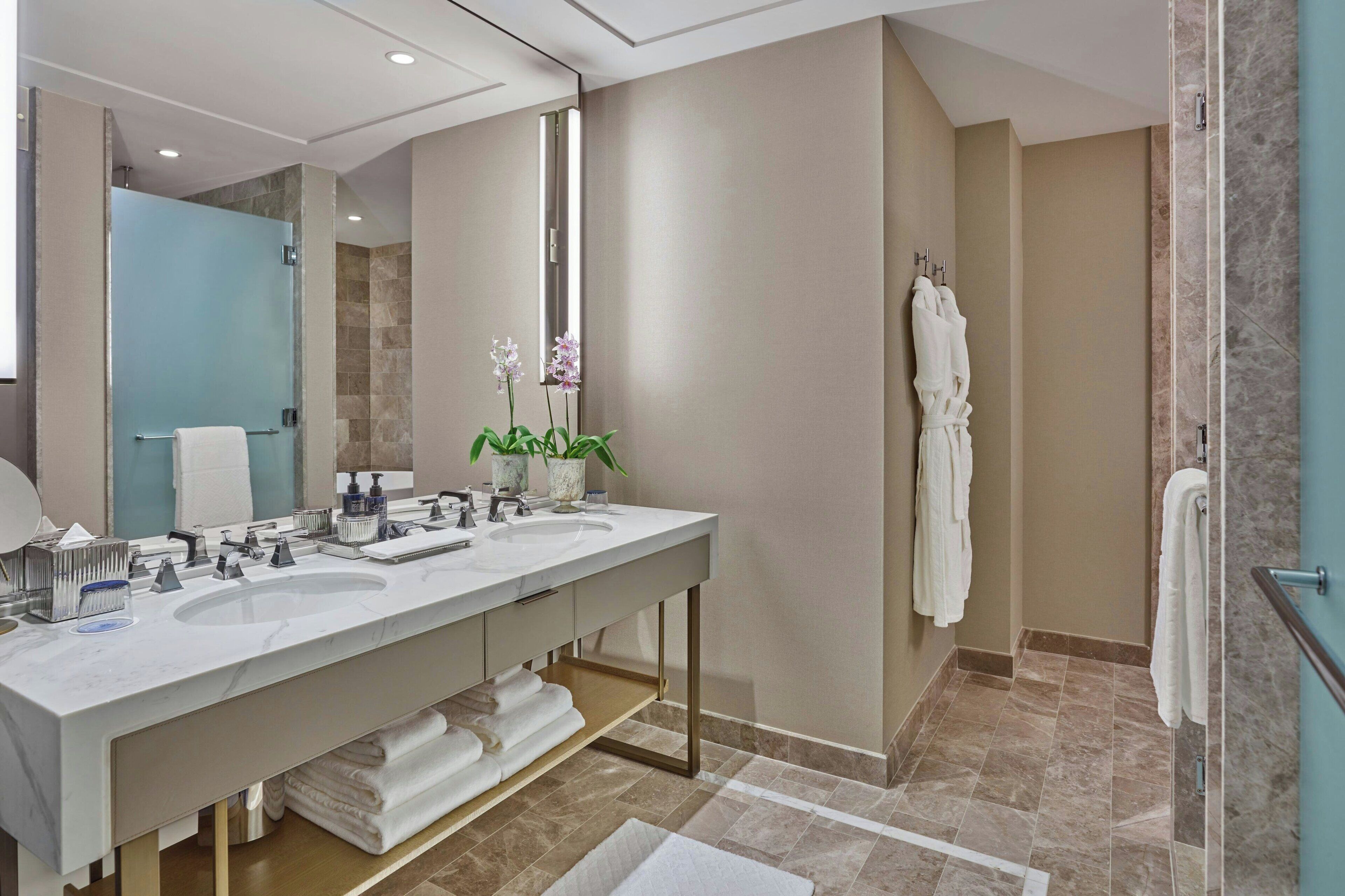 A modern bathroom with a dual sink vanity, a large mirror, and a shower area.
