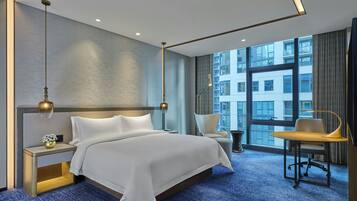 Et moderne hotelværelse med en stor seng, et skrivebord og en stol. Der er et stort vindue med udsigt til bygninger.