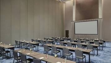 A conference room with rows of tables and chairs, a large screen, and a carpeted floor.