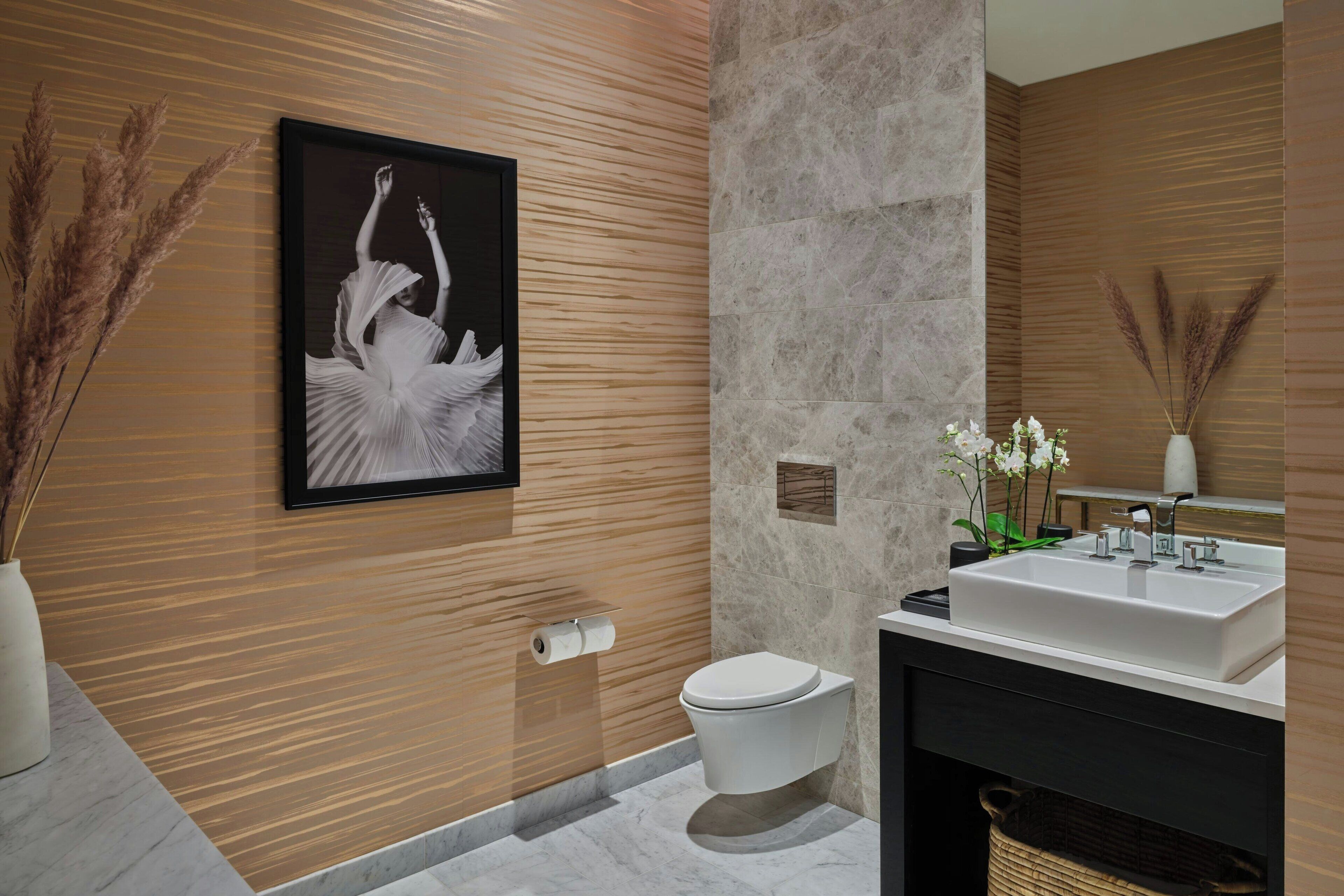 A modern bathroom with a marble floor, a white sink, and a toilet. There is a framed picture on the wall and a vase with dried plants.