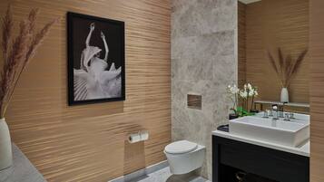 A modern bathroom with a marble floor, a white sink, and a toilet. There is a framed picture on the wall and a vase with dried plants.