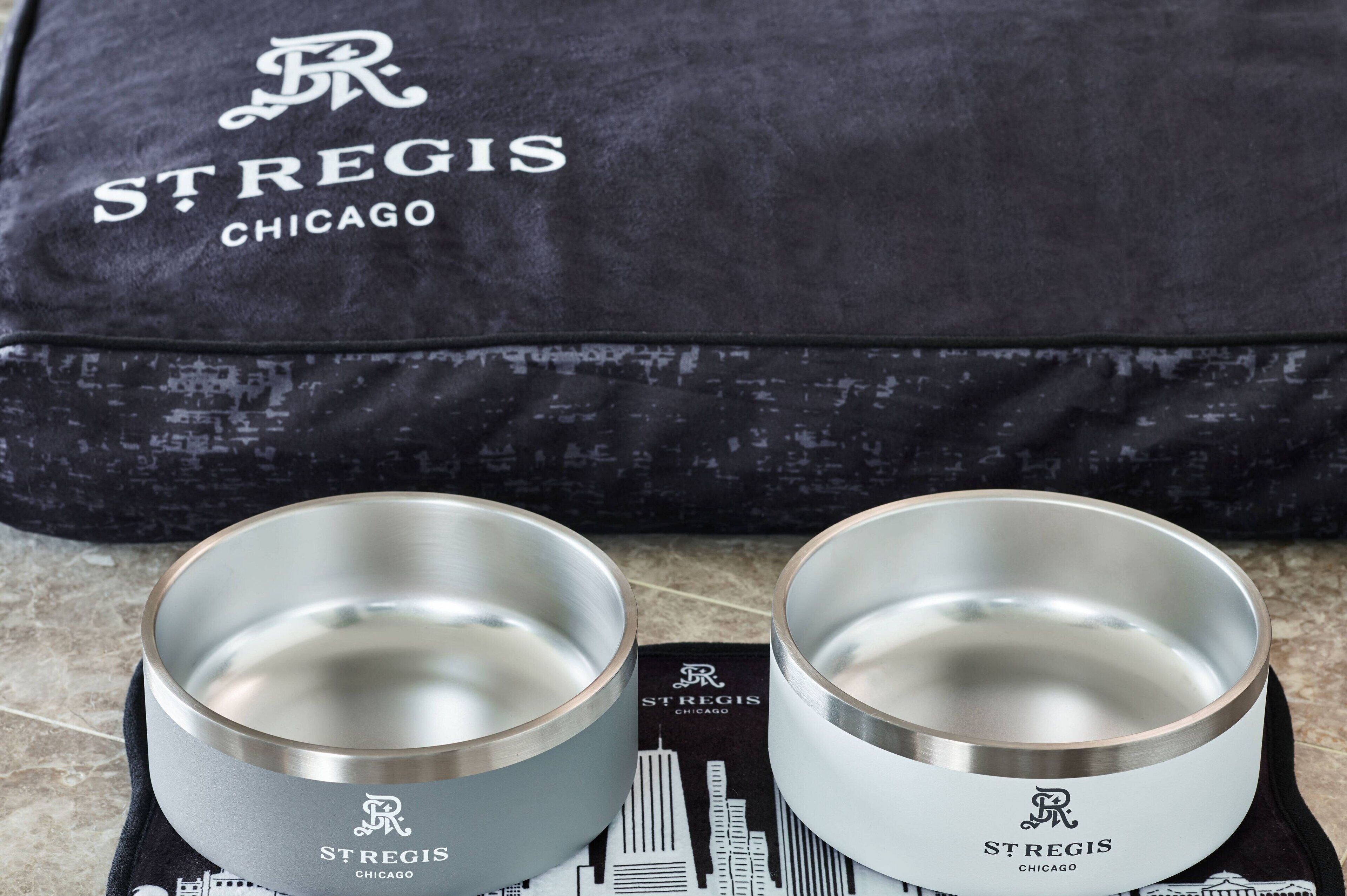 Two stainless steel bowls with the St. Regis Chicago logo, placed on a black cloth with a cityscape print.