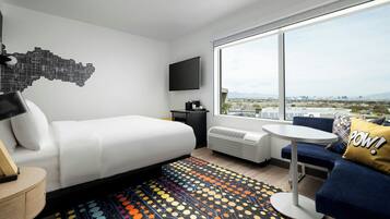 A modern hotel room with a bed, a sofa, a small table, a TV, and a large window offering a city view.