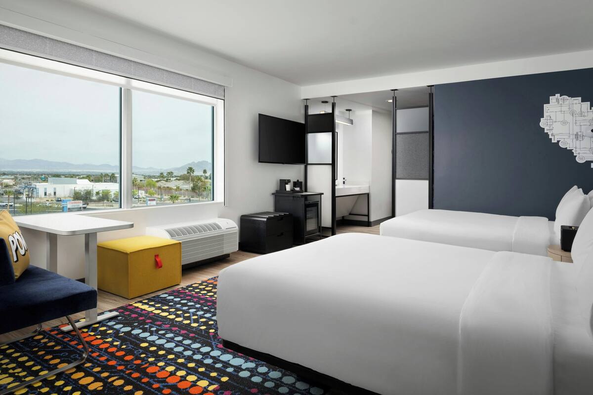 A modern hotel room with a large window, a bed, a desk, and a TV.