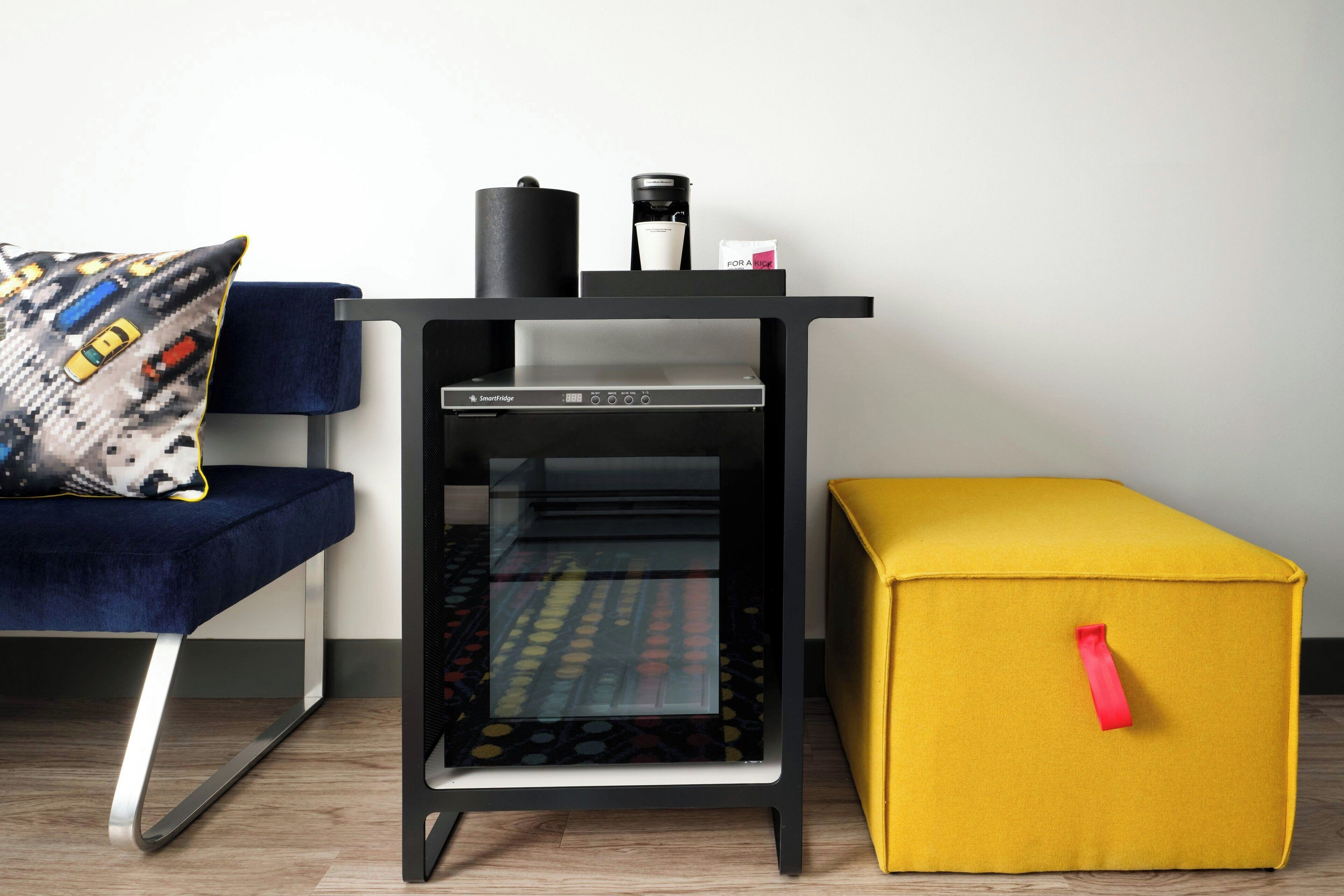 Un espacio habitable moderno con un juego de mobiliario negro y amarillo, que incluye un sofá, una cafetera y un refrigerador SmartFridge.