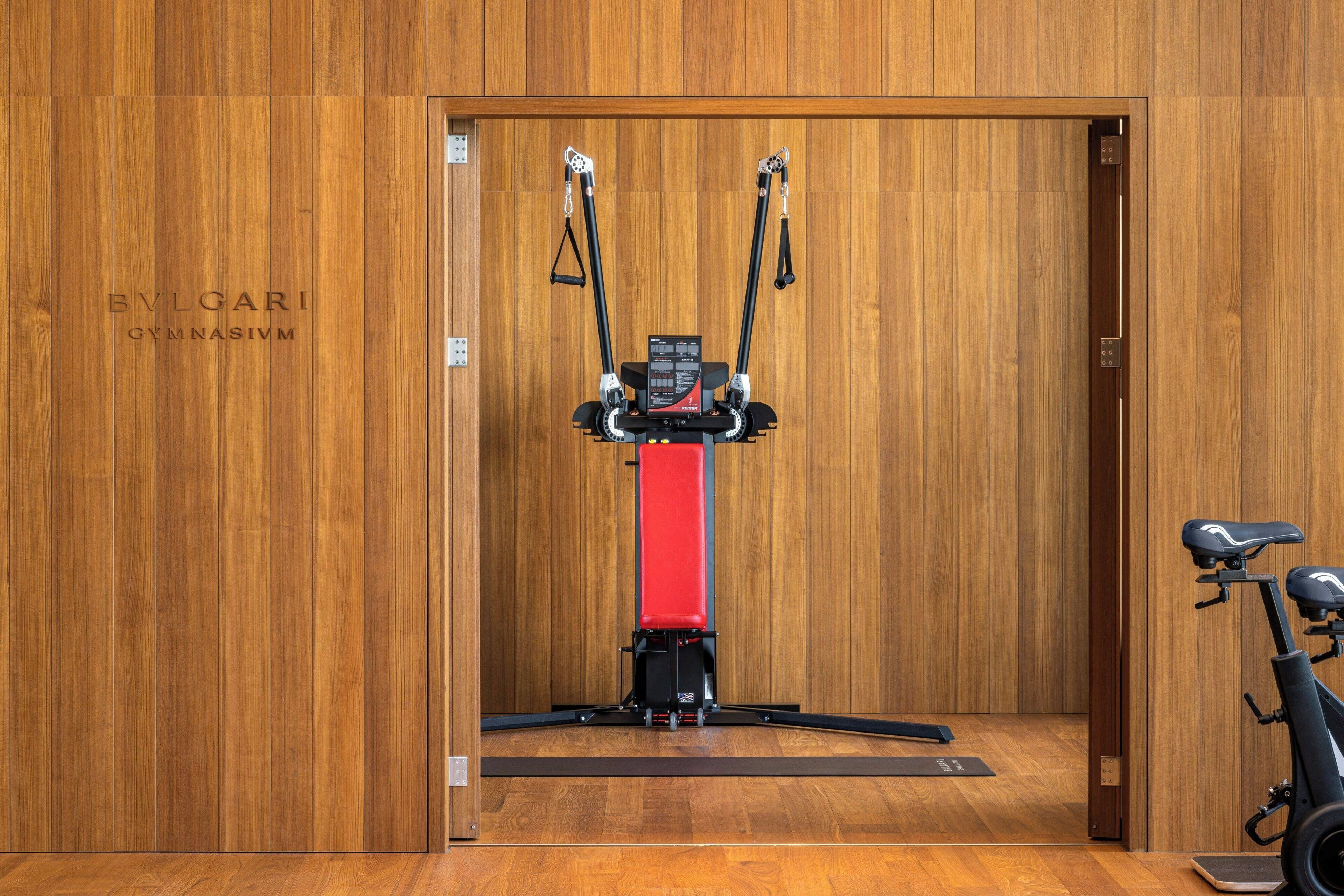Un gimnasio con pared de madera, una máquina de ejercicio roja y una bicicleta estática.