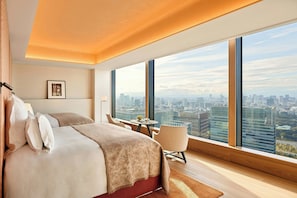 Une chambre d’hôtel moderne dotée d’un grand lit, d’un coin salon et offrant une vue sur la ville grâce à de grandes fenêtres.