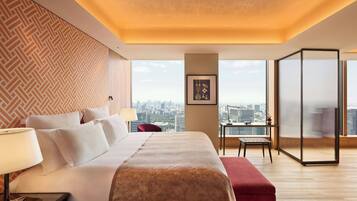 A hotel room with a large bed, a desk, a chair, and a view of the city.