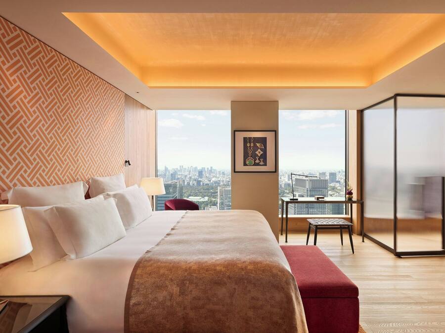 A hotel room with a large bed, a desk, a chair, and a view of the city.