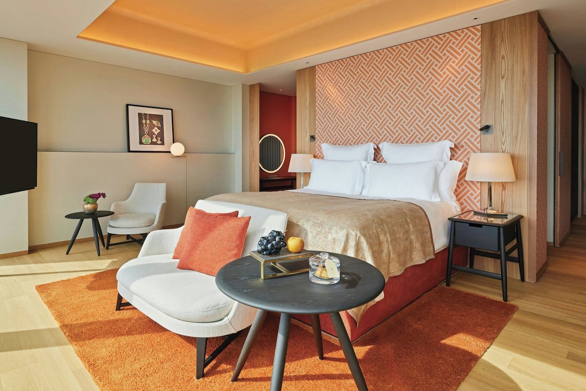 A modern hotel room with a large bed, two bedside tables, a round coffee table, a sofa, and a TV.