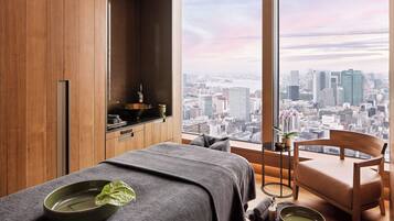 A modern room with a large window, wooden paneling, a massage table, a wooden chair, and a city view.