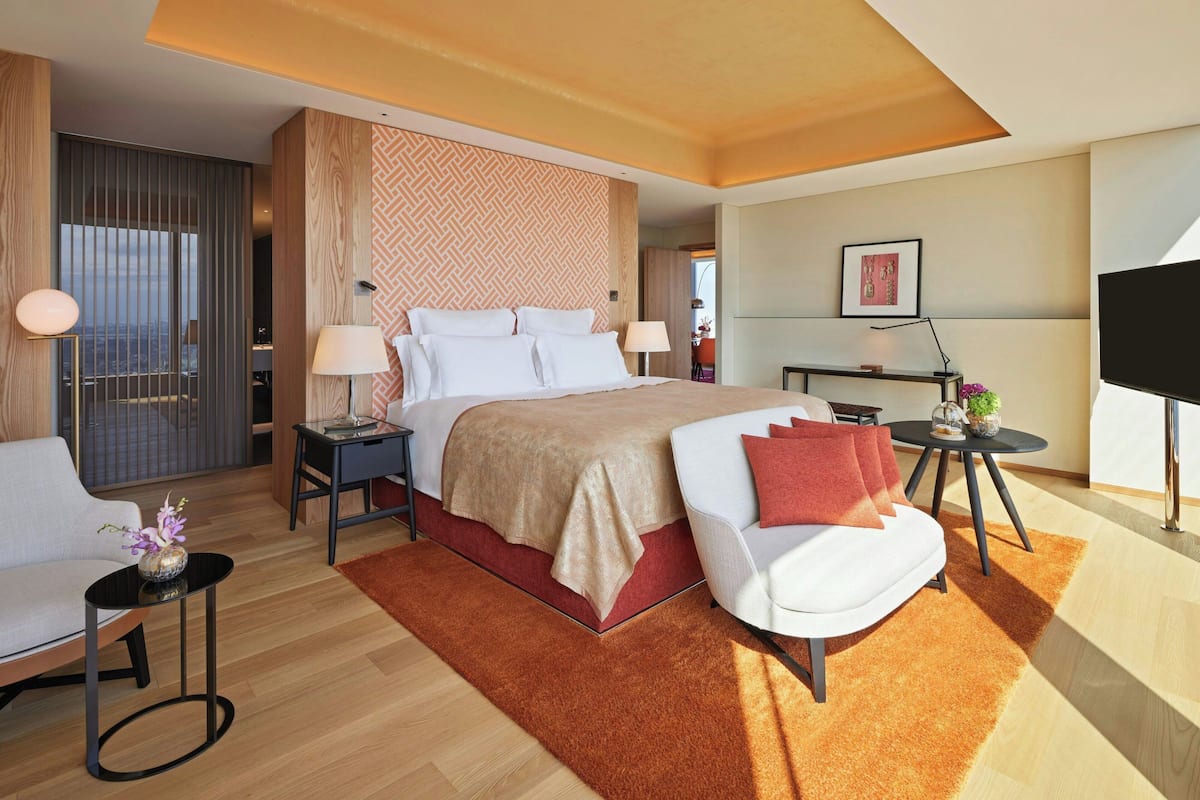 A modern hotel room with a large bed, a sofa, a desk, and a TV.