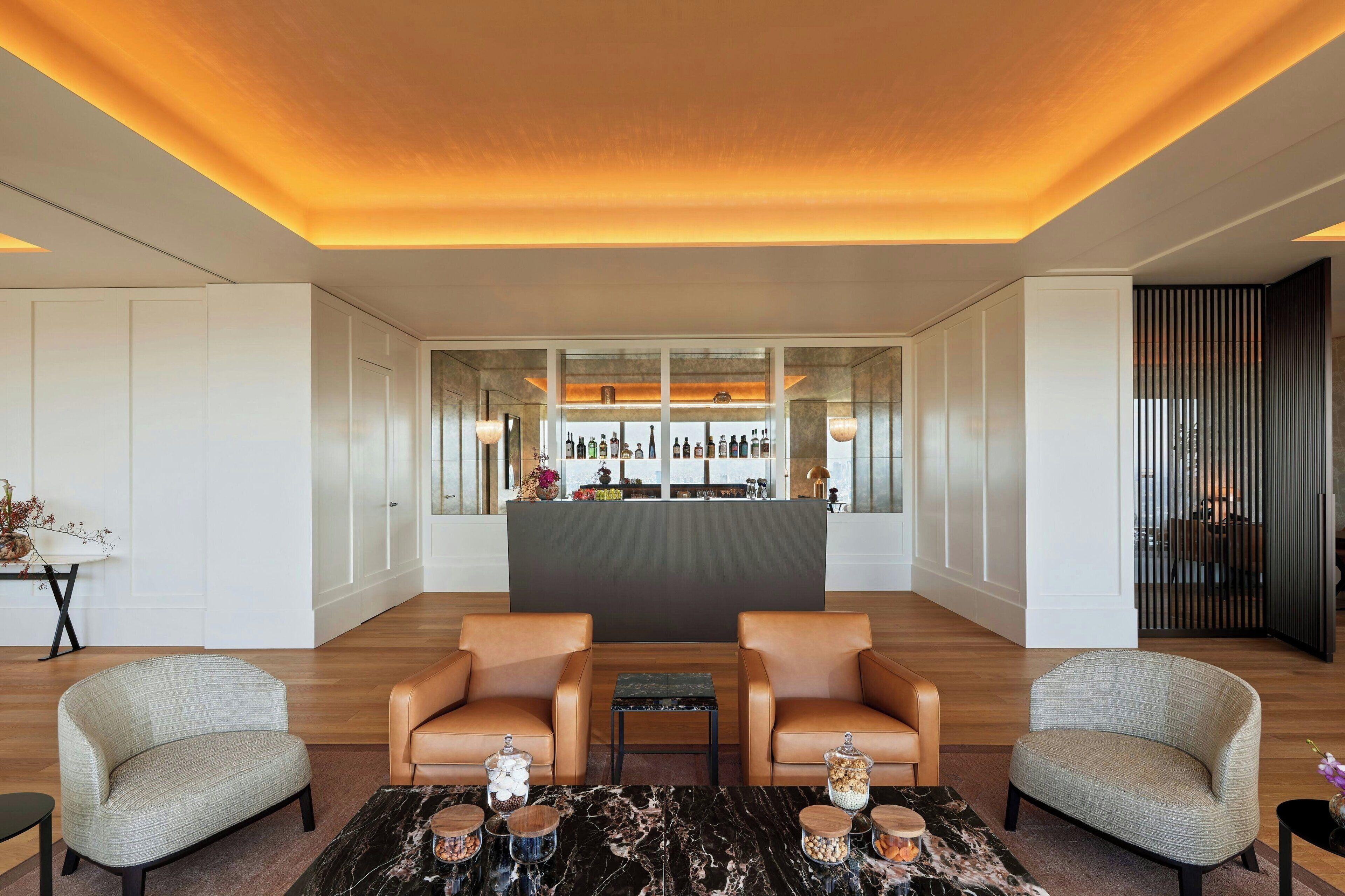 A lobby with two leather armchairs, a marble coffee table, and a bar area with bottles and a cash register.
