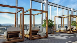 Eine Dachterrasse mit Holzliegen, Blumentöpfen und Blick auf die Stadt.