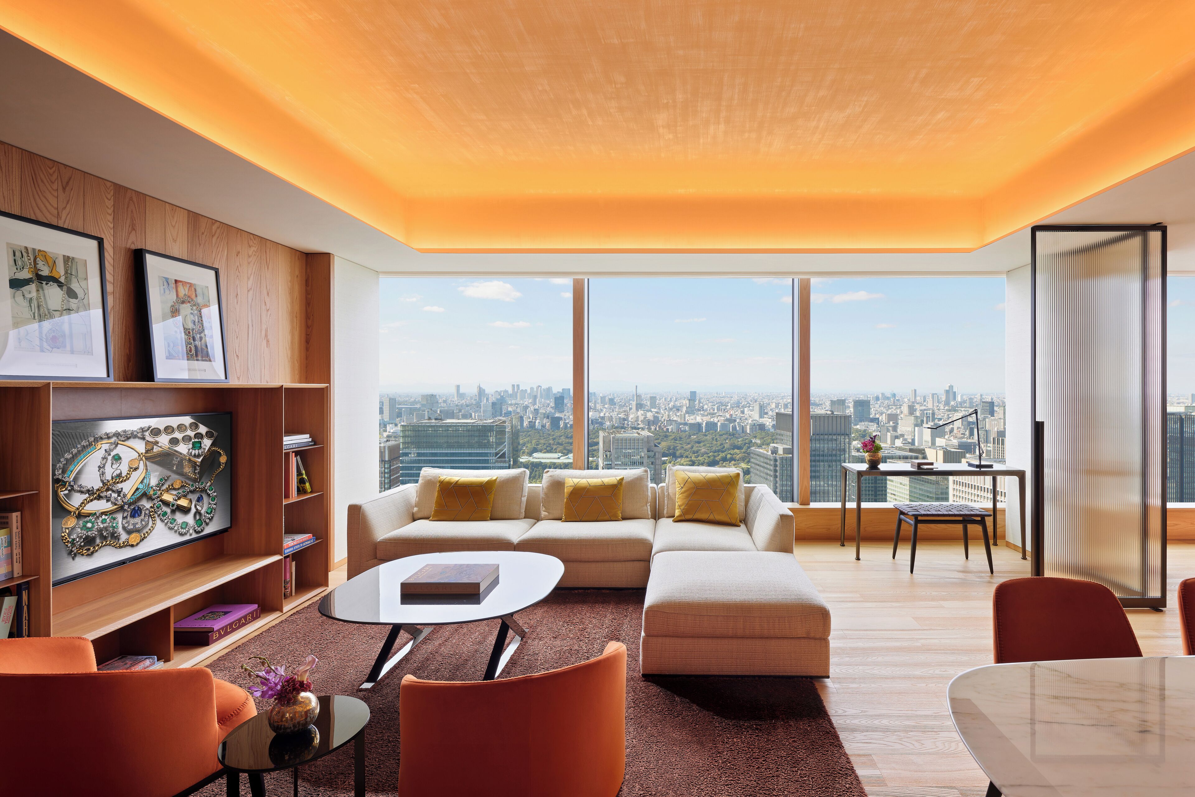 A modern living room with a city view, featuring a sofa, chairs, a coffee table, and a bookshelf.