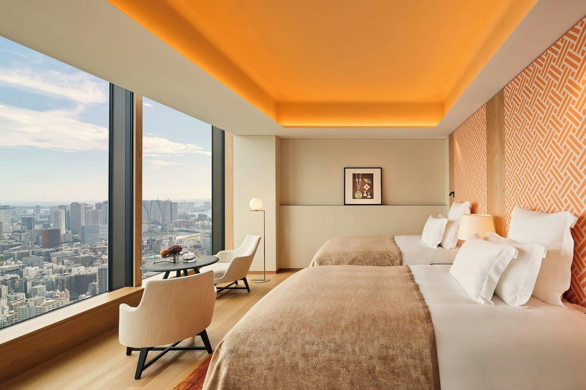 A hotel room with a city view, a bed, a chair, a table, and a lamp.