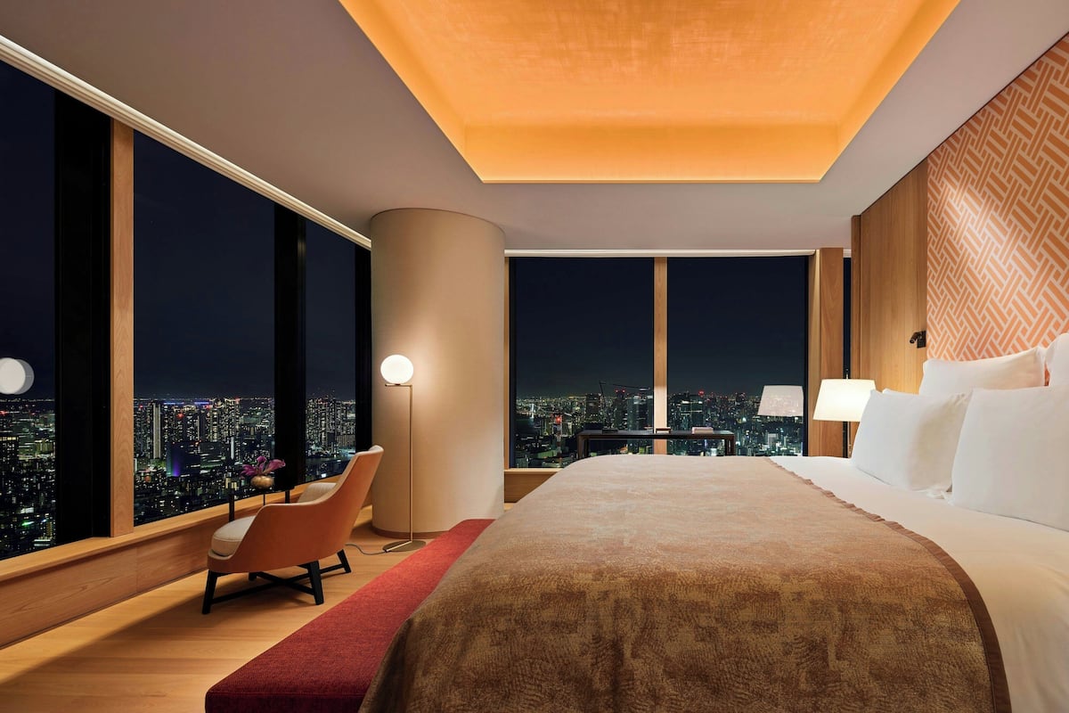 A modern hotel room with a large bed, a desk with a chair, and a view of the city at night.