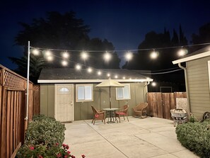 Ein Garten mit Terrasse, Tisch, Stühlen, einem Gartenhaus und Lichterketten.