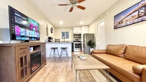 Una sala de estar moderna con un sofá de cuero marrón, una mesa de centro de madera y un televisor que muestra un servicio de streaming. Se observa un ventilador de techo, y el piso es de madera.