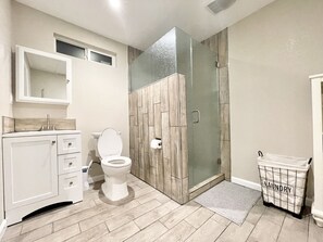 Ein Badezimmer mit Toilette, Waschtisch, Duschkabine mit Glastür und Wäschekorb.