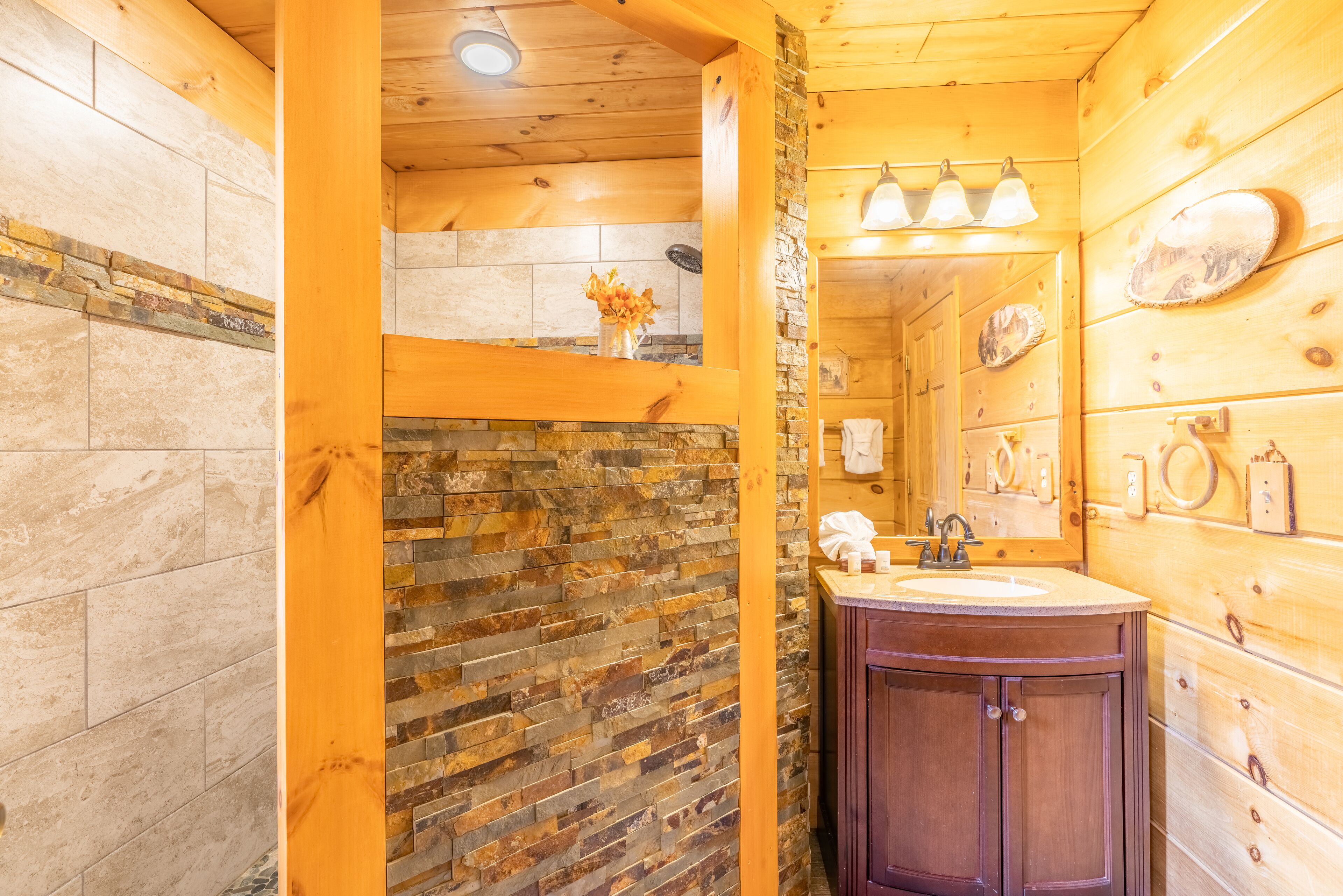 A wooden cabin bathroom with a stone wall, wooden cabinets, and a sink.