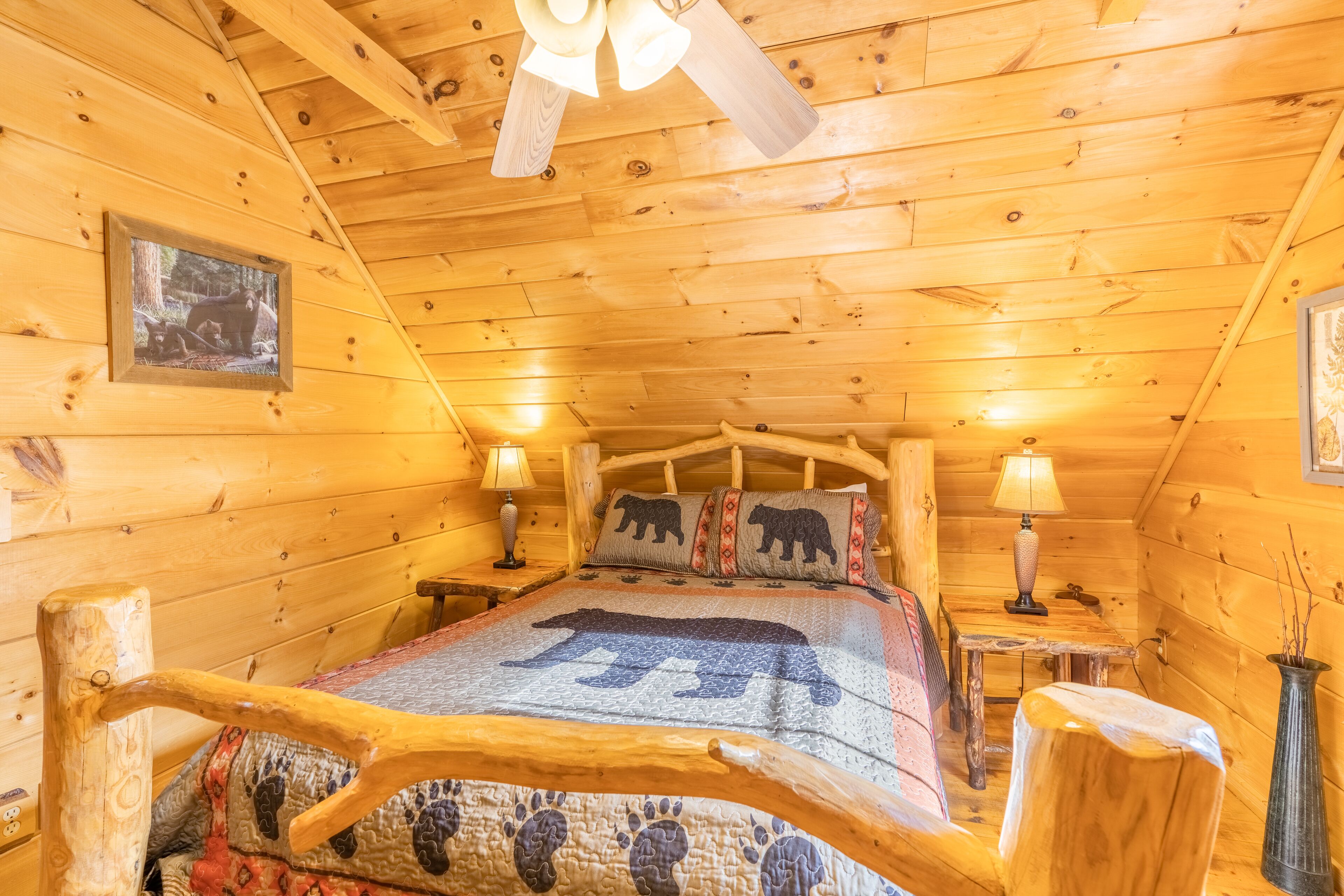 Une chambre à coucher dans un chalet en bois, avec un lit agrémenté d’une couvre-lit à motifs d’ours, deux lampes de chevet et un tableau encadré au mur.