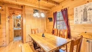 A wooden cabin interior with a dining table, chairs, a chandelier, and a window with curtains. - Bearway to Heaven #2 (Pigeon Forge)