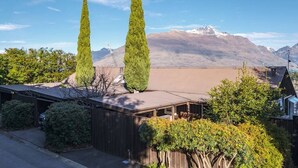 A residential area with two tall, narrow trees, a house with a sloped roof, and a mountain range in the background. - Stunning Views with a Fantastic Location! (Queenstown)
