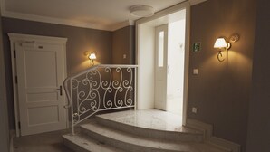 Un escalier orné d’une rampe en métal décorative, une porte blanche et des luminaires fixés au mur.
