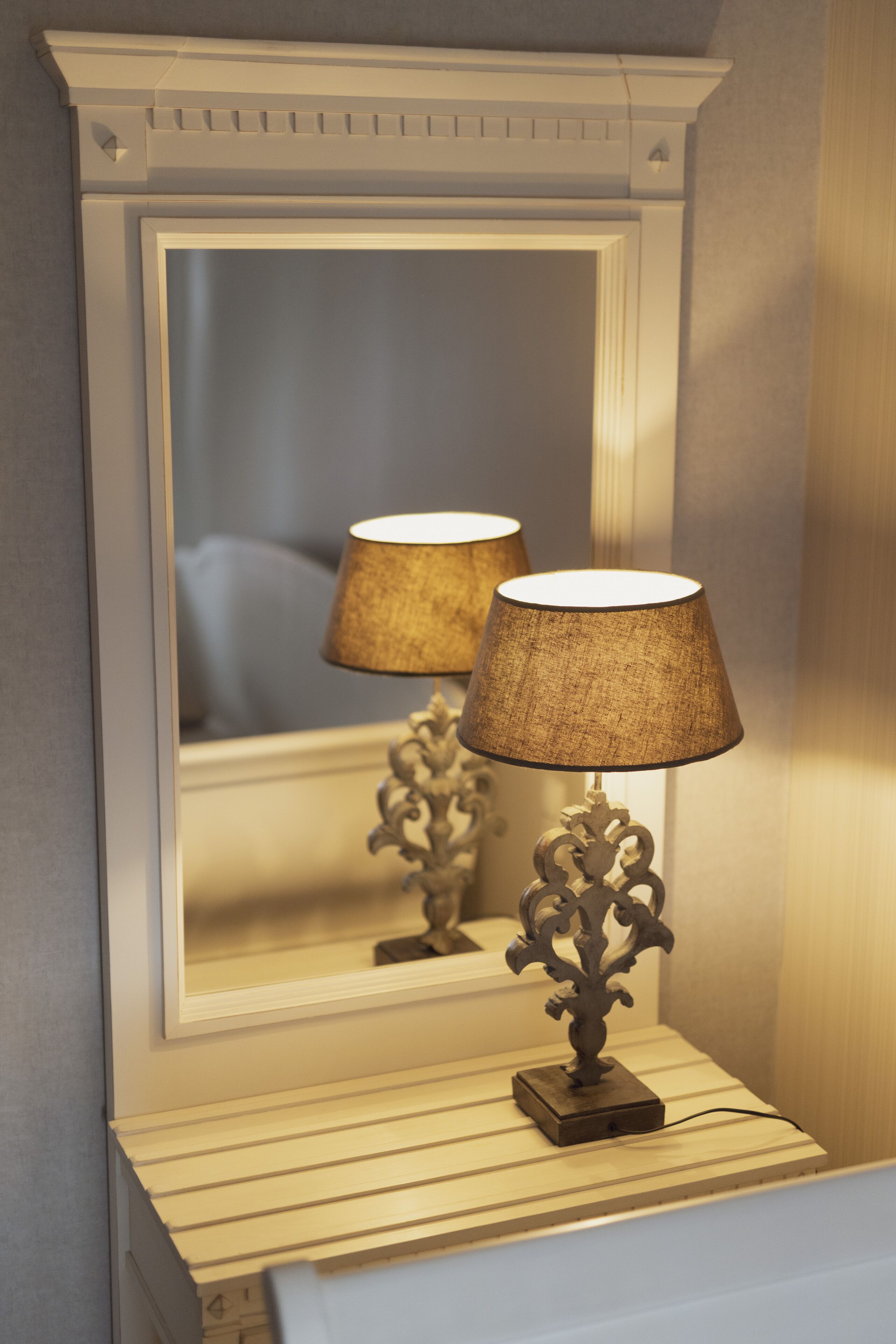 Un miroir avec un cadre décoratif et une lampe de table dotée d’un abat-jour texturé.