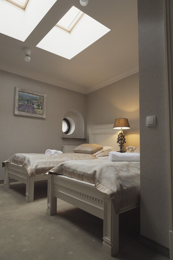 A bedroom with two beds, skylights, a painting, a round mirror, a lamp, and a telephone.