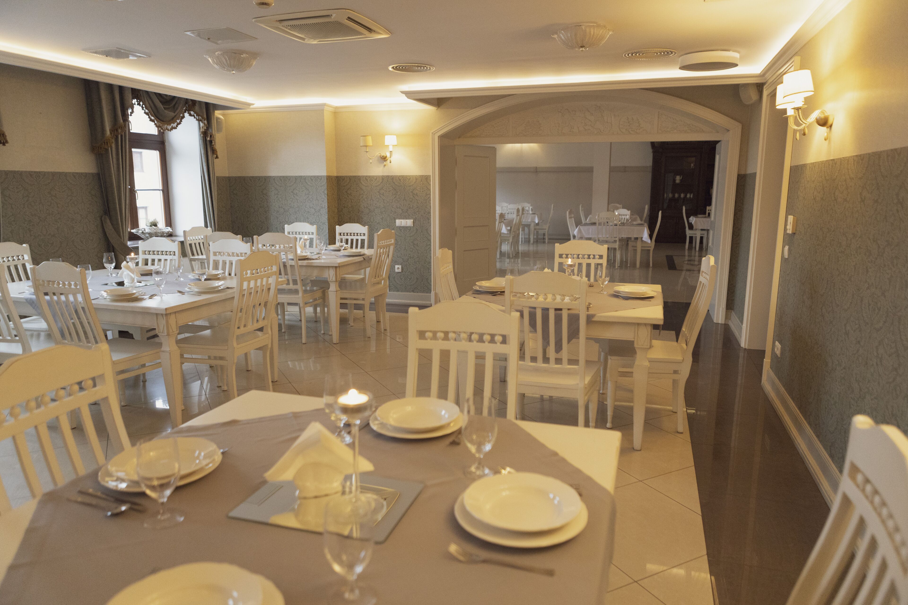 Uma sala de jantar com mesas postas, cadeiras e um candelabro.