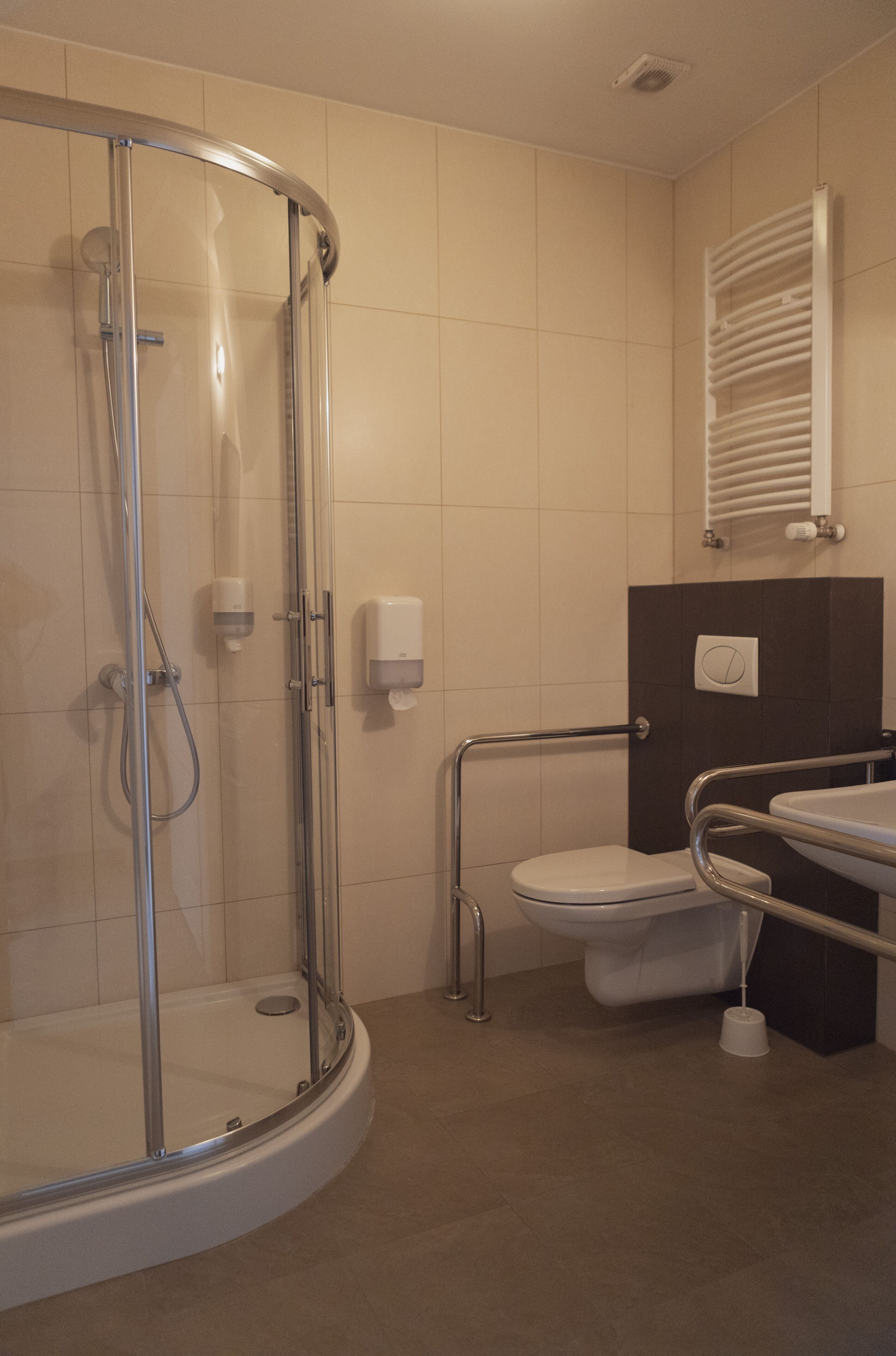 A bathroom with a glass-enclosed shower, a toilet with a handrail, and a sink with a mirror.