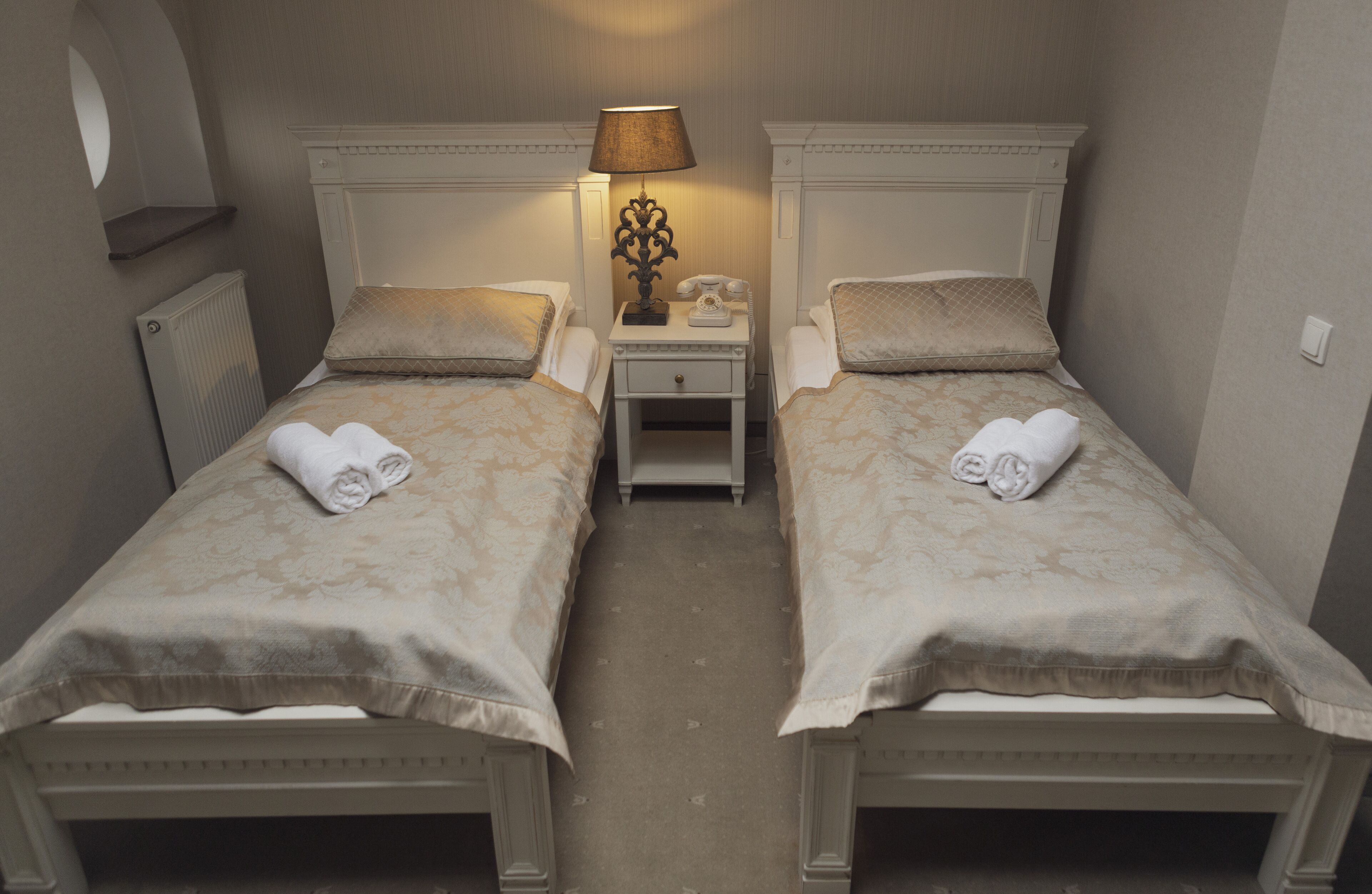 A twin room with two beds, a nightstand with a lamp, and a radiator.