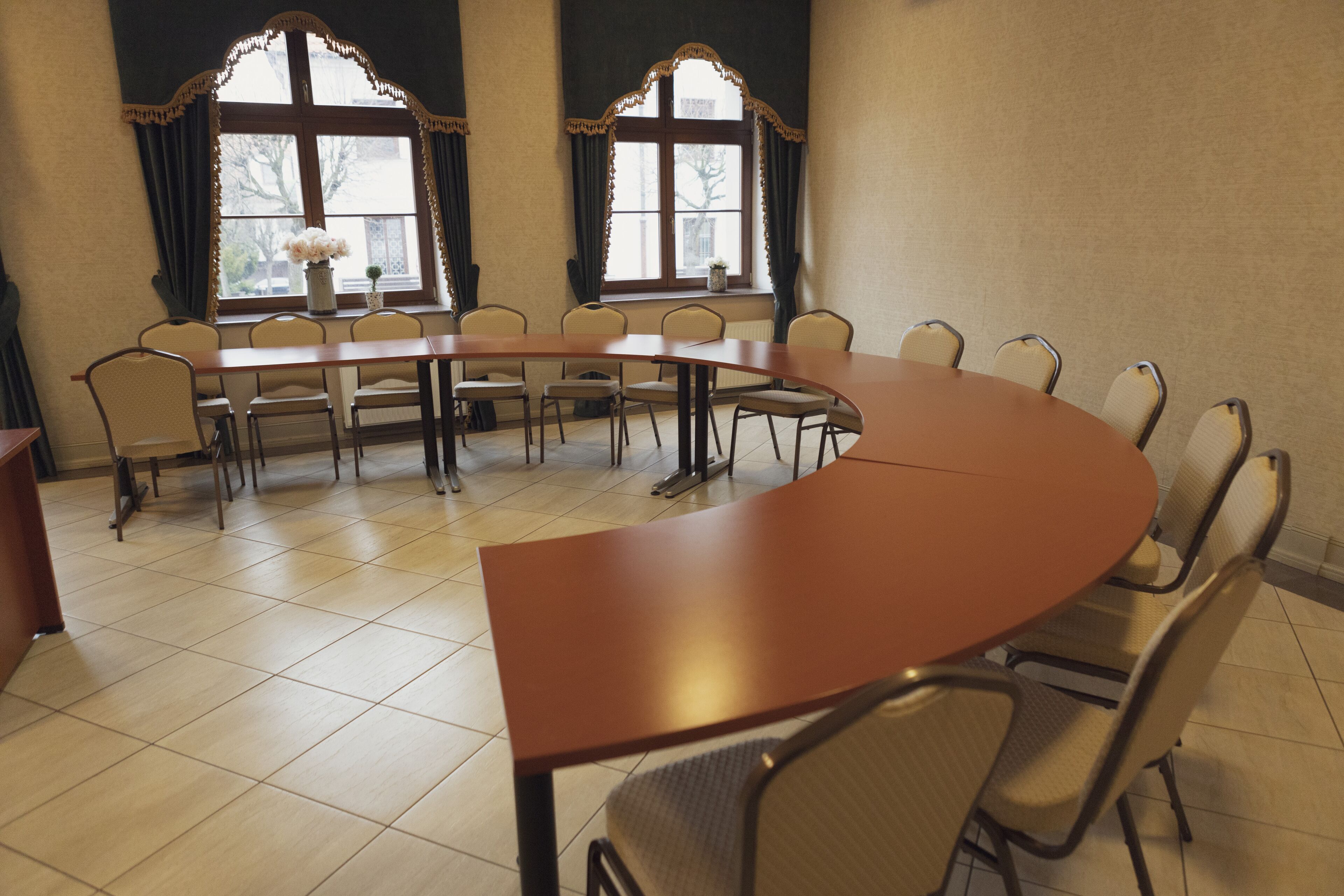 Une salle de conférence dotée d’une grande table ovale et de plusieurs chaises, de grandes fenêtres avec des rideaux et d’un sol carrelé.