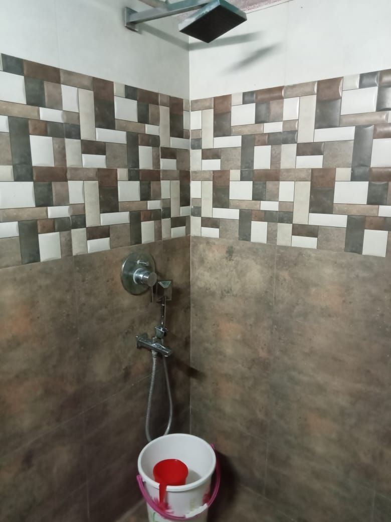 Zona de ducha con pared de azulejos, un cabezal de ducha y un cubo.