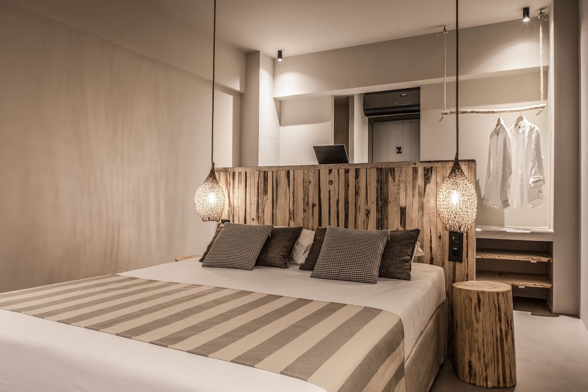 Une chambre moderne avec un grand lit, une tête de lit en bois et une armoire intégrée avec des vêtements suspendus.