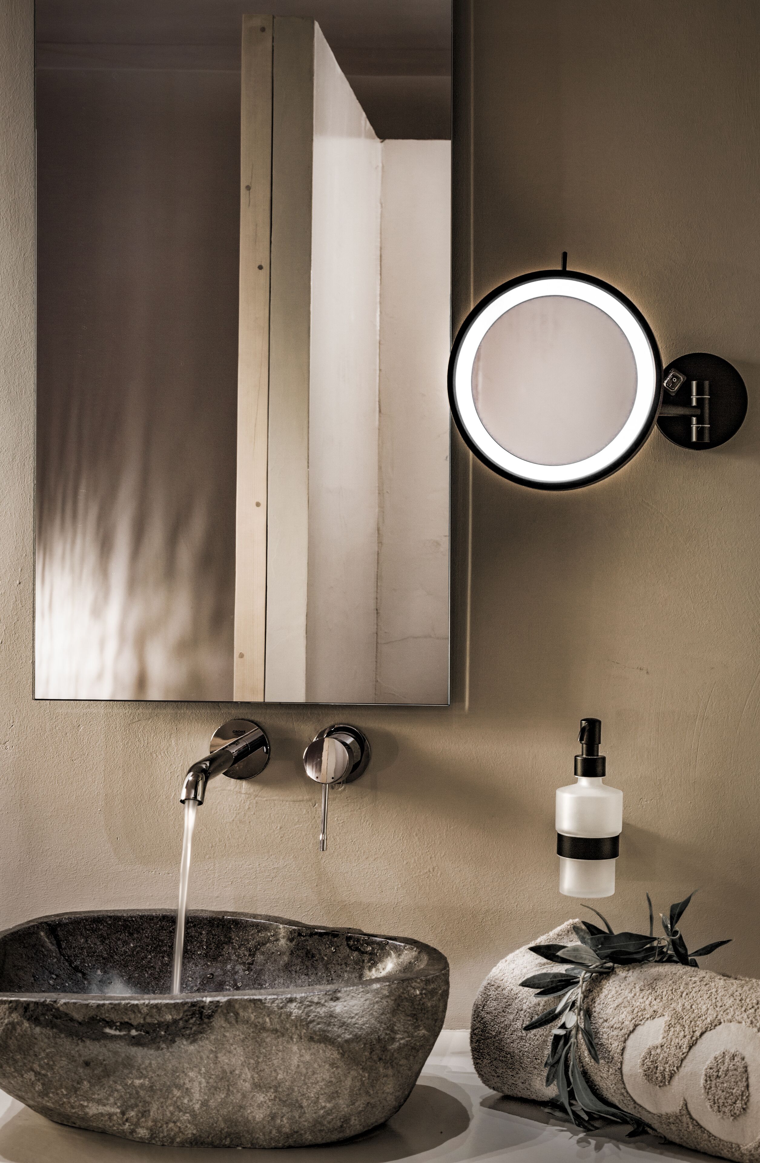 A bathroom with a stone sink, a mirror with a light, and a towel with a leaf design.