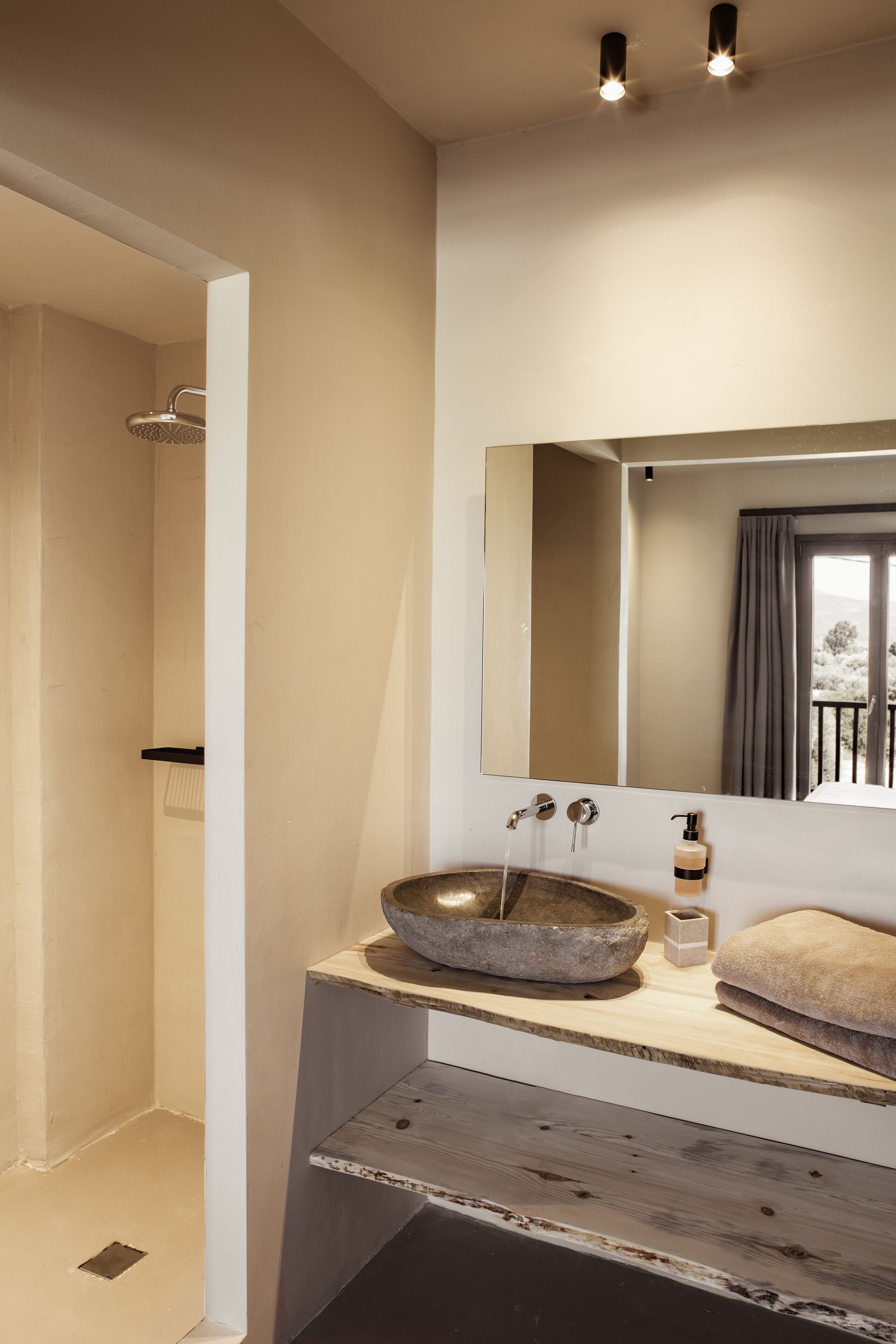 A modern bathroom with a stone basin sink, a large mirror, and a shower area.