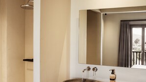 A modern bathroom with a stone basin sink, a large mirror, and a shower area.