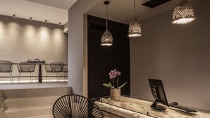 Un mostrador de recepción moderno con superficie de madera, una computadora y un florero con flores. Se ven sillas y una escalera al fondo.