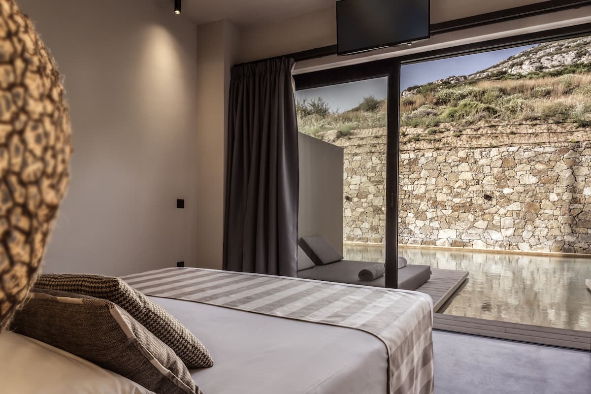 Une chambre à coucher avec un lit, une grande fenêtre et un mur en pierre à l’extérieur.