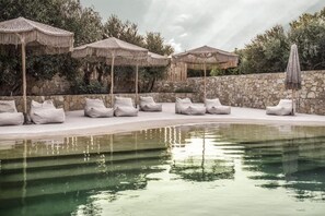 Un espace piscine agrémenté de chaises longues et de parasols, entouré de murs en pierre et de verdure.