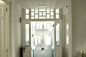 Corredor com portas brancas, uma porta central com janela e um radiador na parede direita.