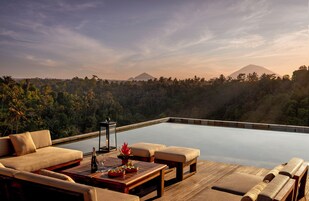 A poolside area with a sofa, chairs, and a table with a bottle and flowers.